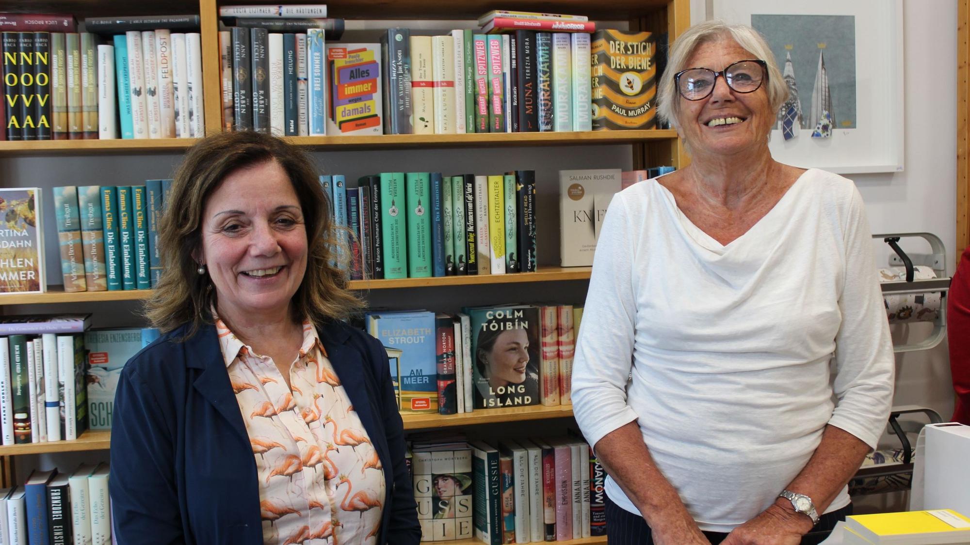 Die beiden Frauen stehen vor einem Regal voller Bücher.
