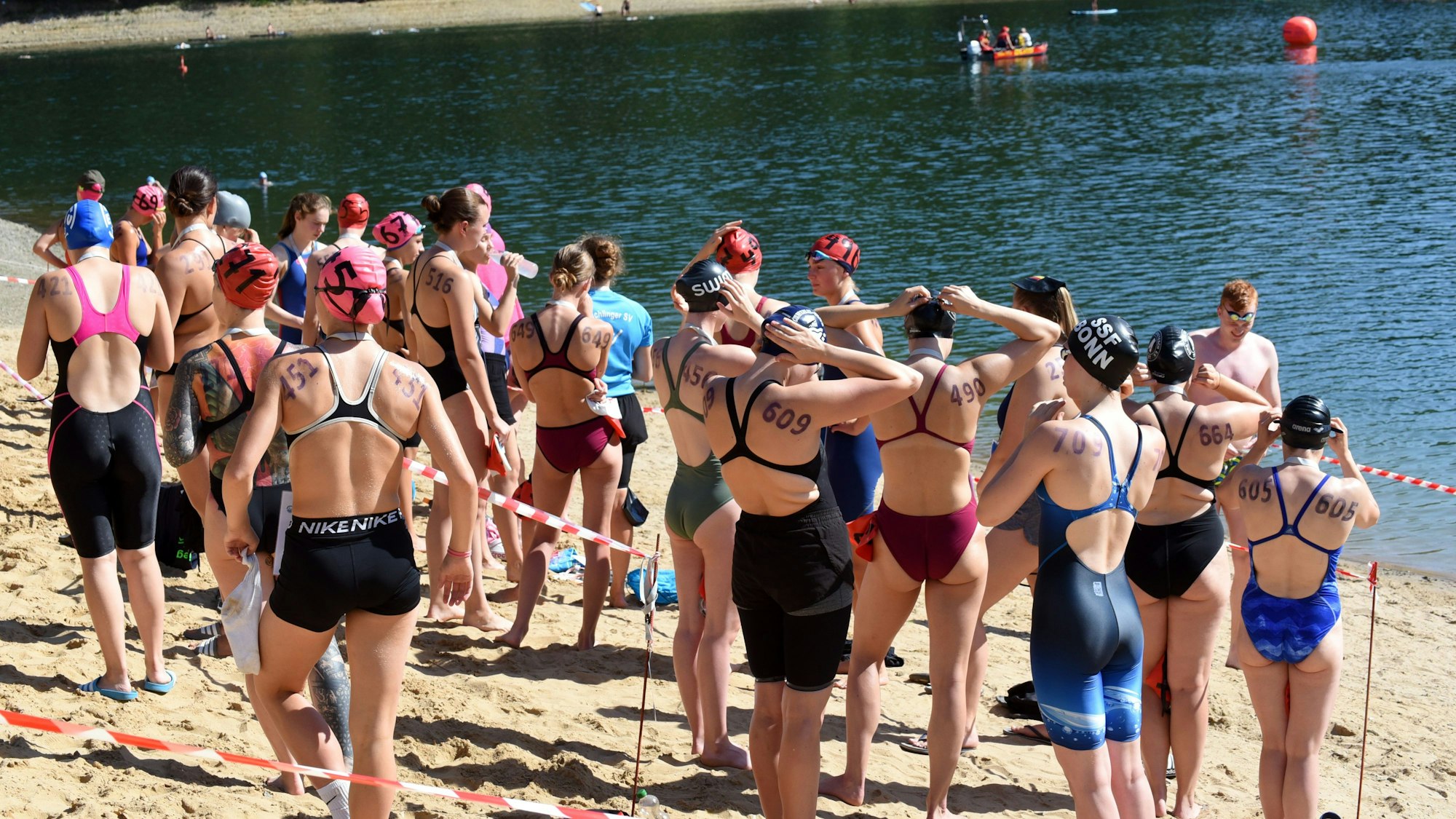 Zahlreiche Schwimmer stehen kurz vor dem Start eines Wettbewerbs am Strand an einer Talsperre.