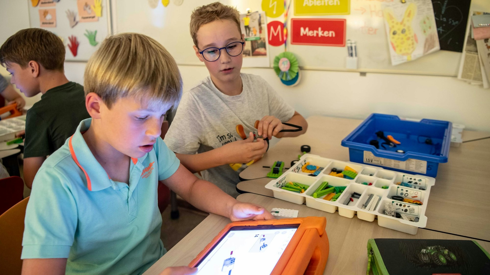 Zwei Grundschüler schauen auf den leuchtenden Bildschirm eines iPads, das auf einem Tisch liegt.