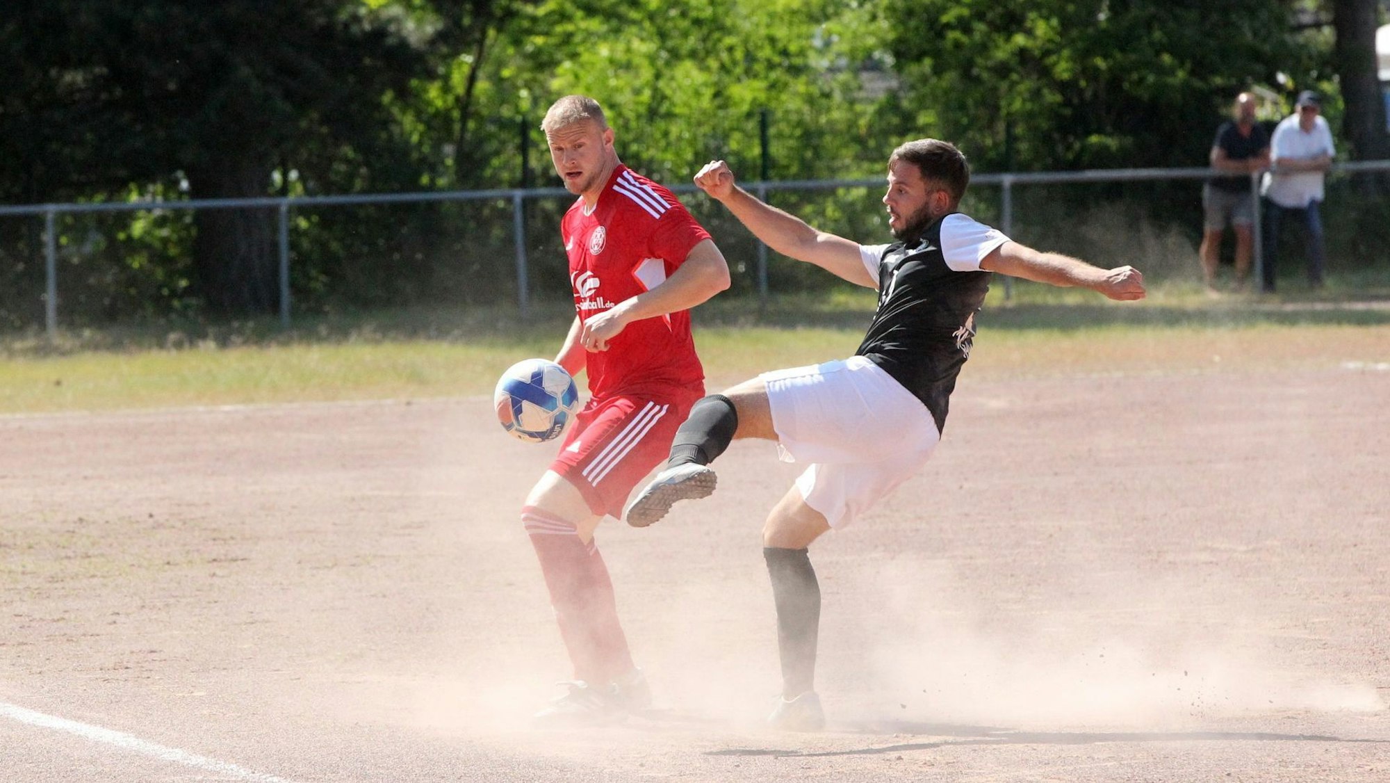 Zwei Fußballer kämpfen auf einem Aschenplatz um den Ball. Es staubt gewaltig,