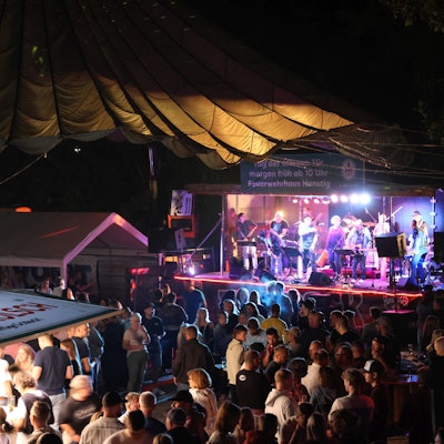 Ein Band spielt vor Publikum auf einer Bühne. Es ist dunkel.