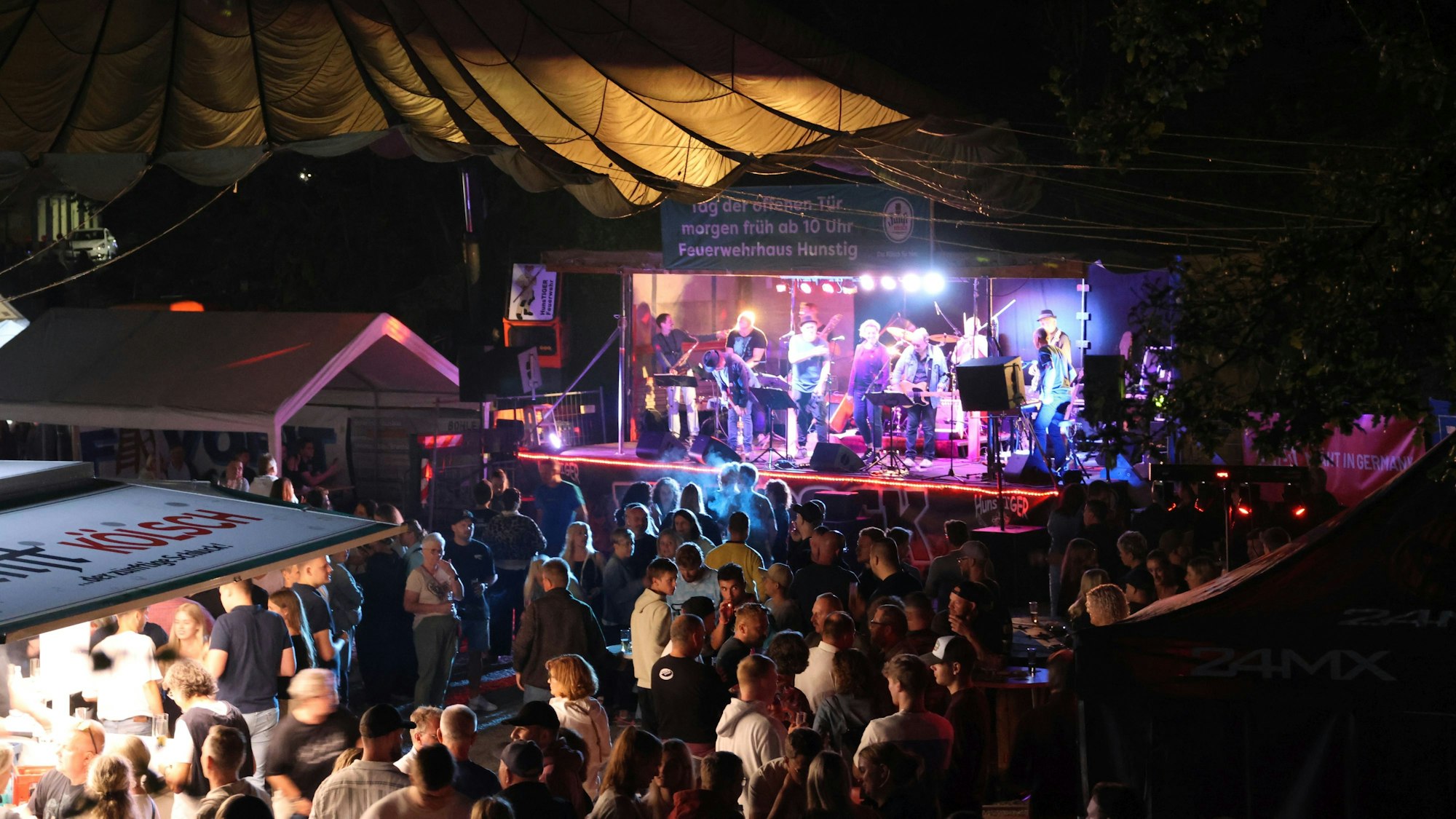 Ein Band spielt vor Publikum auf einer Bühne. Es ist dunkel.