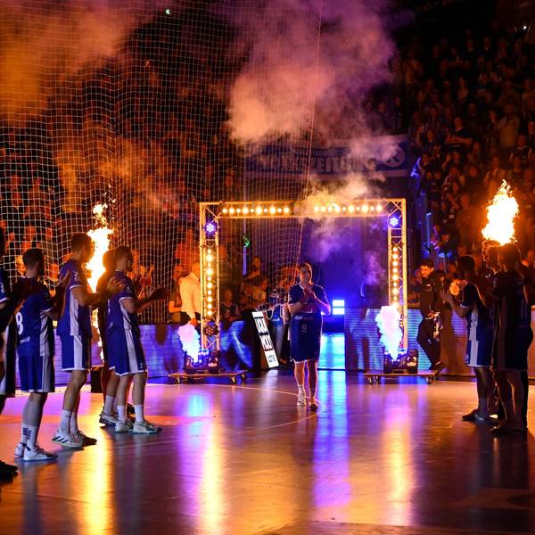 Zu sehen ist eine Szene aus der Einlaufshow einer Handball-Mannschaft mit Feuerwerk.