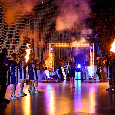 Zu sehen ist eine Szene aus der Einlaufshow einer Handball-Mannschaft mit Feuerwerk.