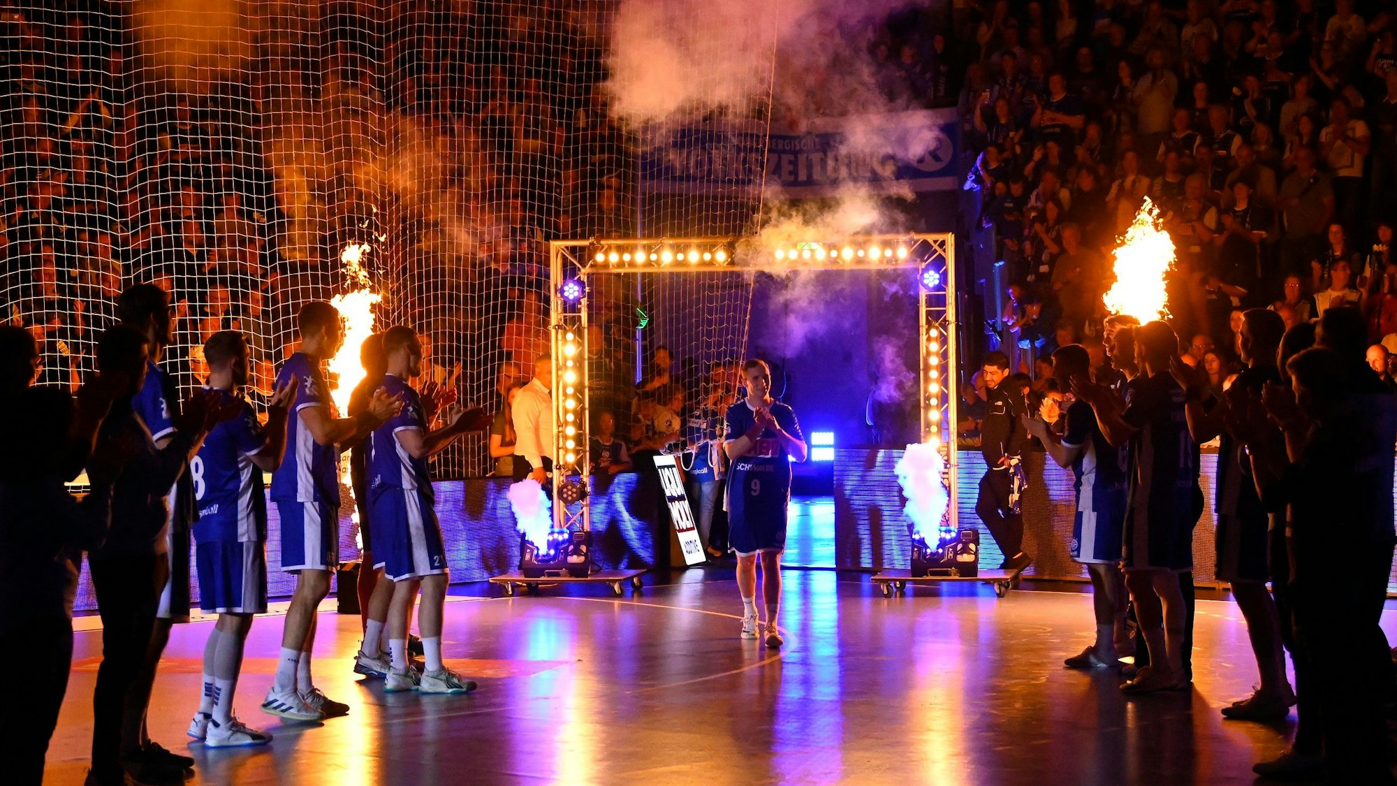 Zu sehen ist eine Szene aus der Einlaufshow einer Handball-Mannschaft mit Feuerwerk.
