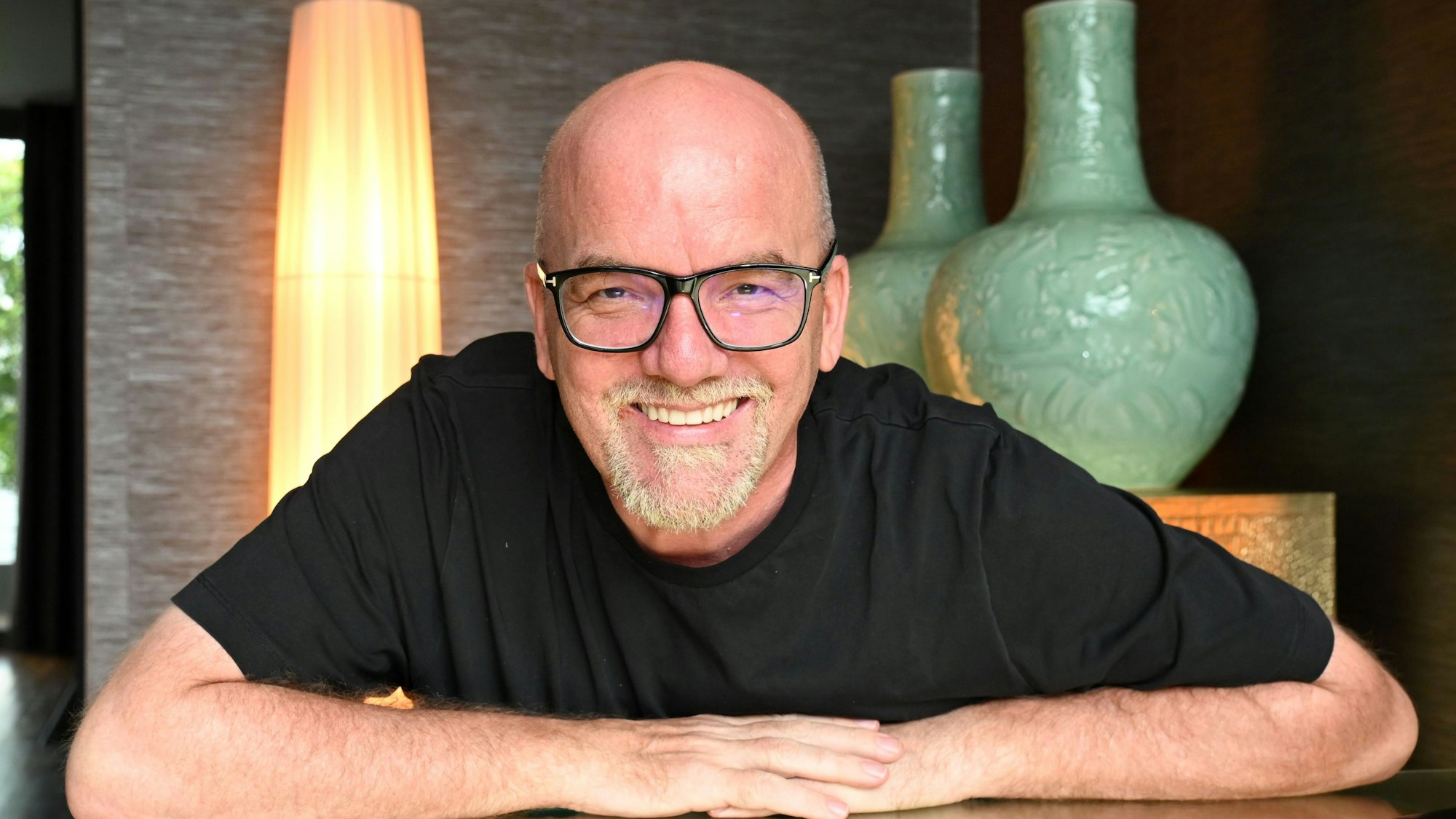 Gerhard Friedle alias DJ Ötzi lehnt sich auf einen Tisch und grinst in die Kamera.