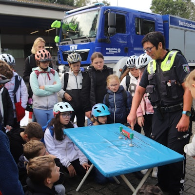 Eine Polizistin erklärt Kindern an einem Tisch eine Verkehrssituation.