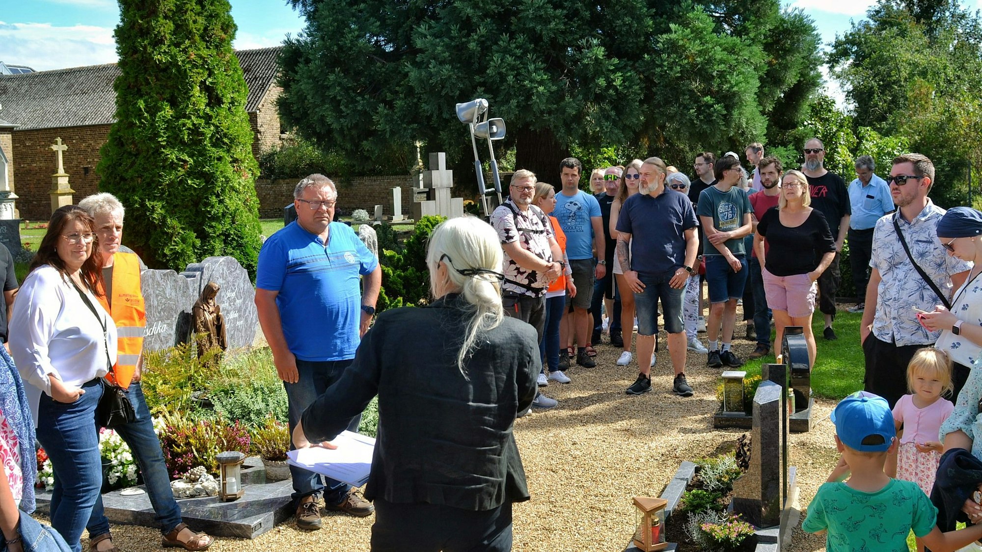 Eine Gruppe von Menschen steht auf dem Friedhof.