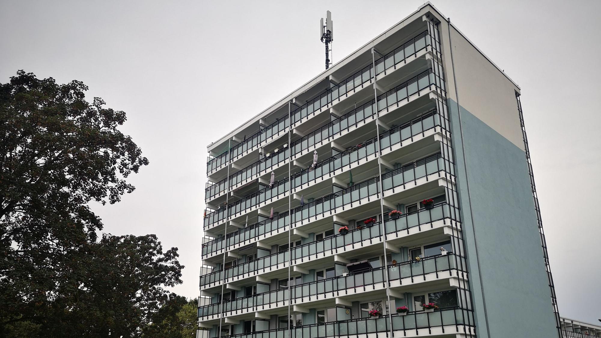 Ein Mehrfamilienhaus vor grauem Himmel. Links steht ein Baum.