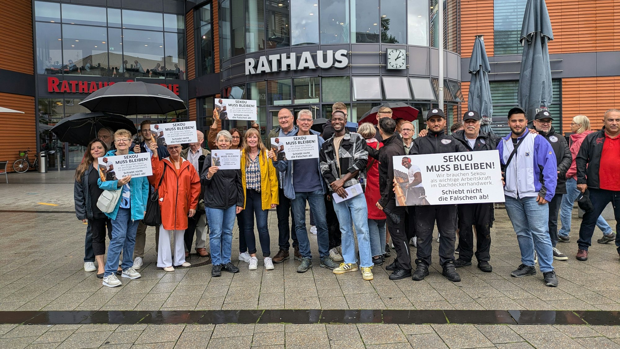 Eine Gruppe von Menschen steht vor einem Rathaus und hält Schilder hoch.