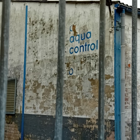 Der Schriftzug der Firma Aqua Control hinter einem Absperrgitter.