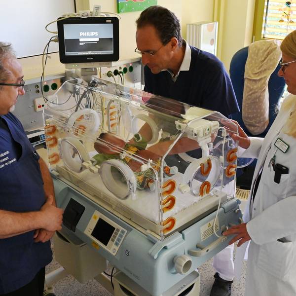 Zwei Männer in blauen Shirts und eine Frau in weißem Arztkittel, Wael Shabanah, Dr. Herbert Schade und Dr. Tatjana Klug betrachten ein neugeborenes Kind auf der Kinderintensivstation im Kreiskrankenhaus Mechernich.