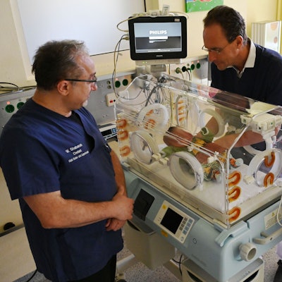 Zwei Männer in blauen Shirts und eine Frau in weißem Arztkittel, Wael Shabanah, Dr. Herbert Schade und Dr. Tatjana Klug betrachten ein neugeborenes Kind auf der Kinderintensivstation im Kreiskrankenhaus Mechernich.