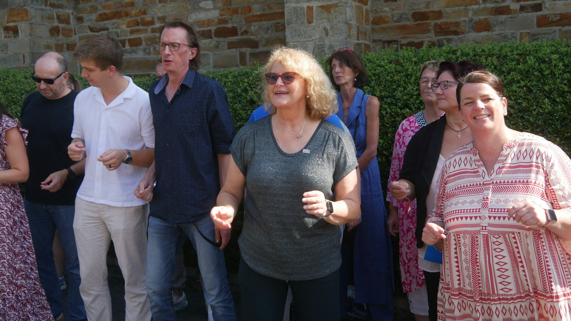 Eine blonde Frau mit Brille in einer Reihe von tanzenden und singenden Menschen.