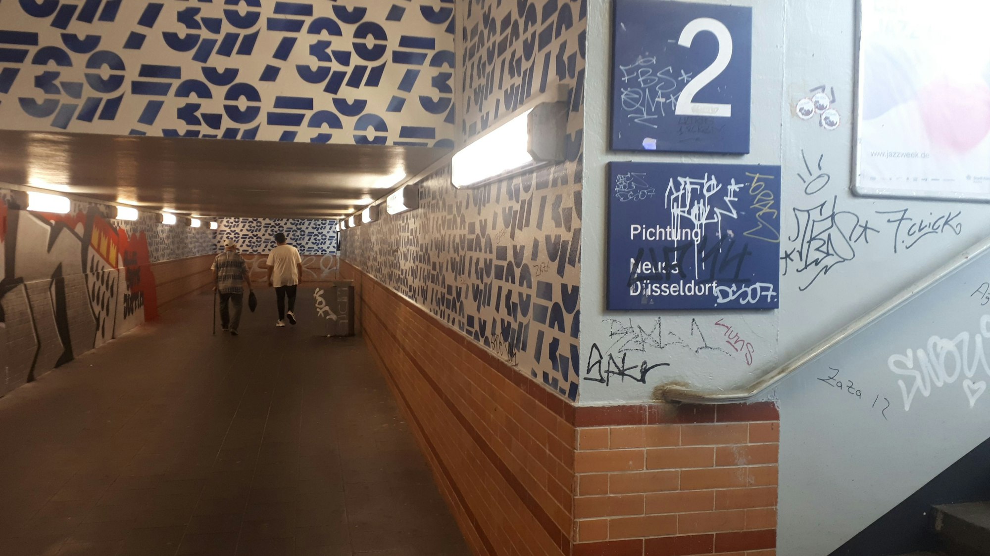 Graffiti allerorten am S-Bahnhof Longerich: Mauern, Wände, Treppenstufen, Lampen und auch Wegweiser-Schilder sind beschmiert.