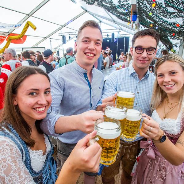 Zwei junge Frauen und zwei junge Männer in Tracht prosten sich mit Maßkrügen zu.