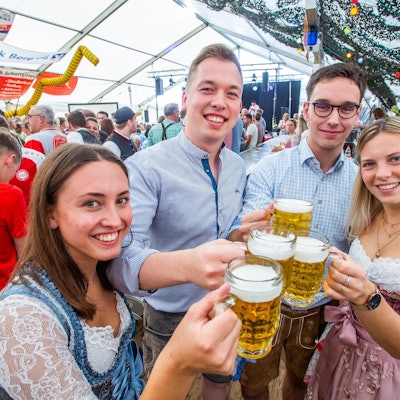 Zwei junge Frauen und zwei junge Männer in Tracht prosten sich mit Maßkrügen zu.
