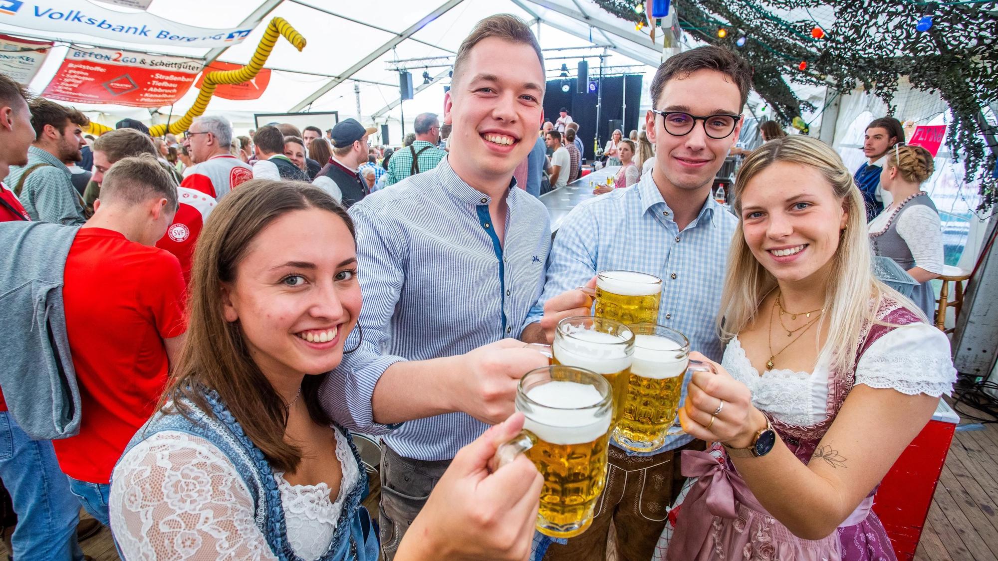 Zwei junge Frauen und zwei junge Männer in Tracht prosten sich mit Maßkrügen zu.