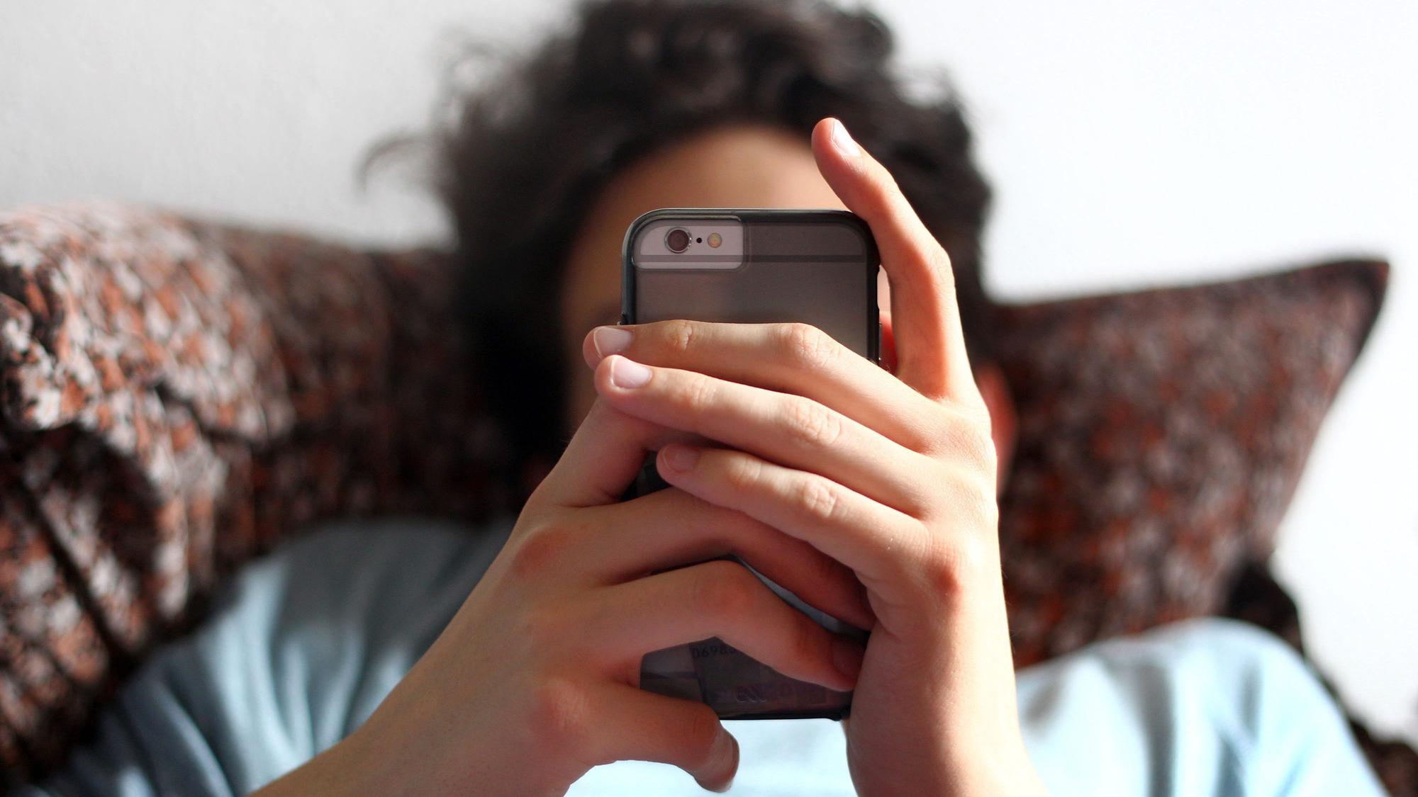 Ein junger Mann blickt auf ein Smartphone.