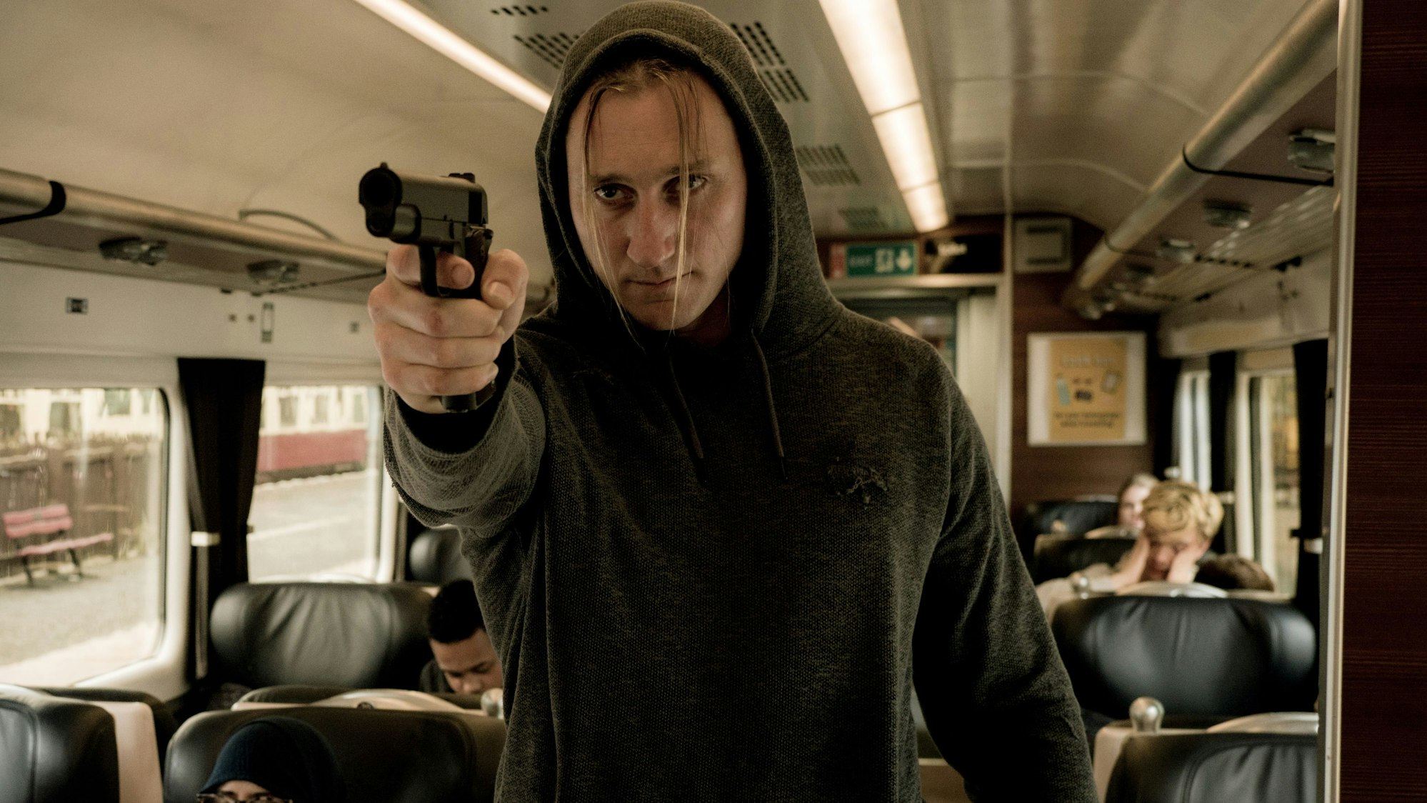 Ian Slade (Liliom Lewald) richtet in einem Zug eine Waffe Richtung Kamera.