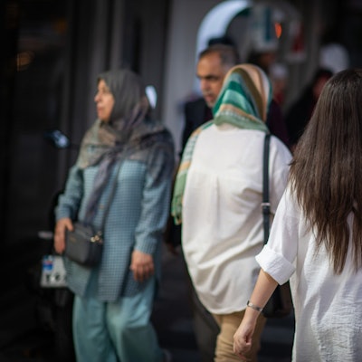 10.07.2023, Iran, Teheran: Eine Frau läuft in Teheran mit offenen Haaren am Abend eine Straße entlang.
