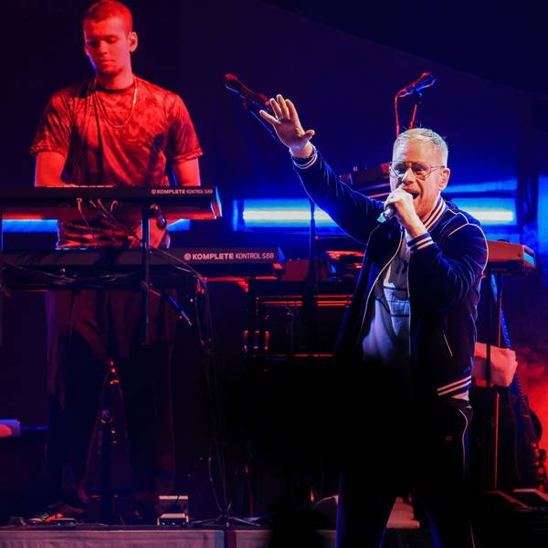 Peter Fox steht singend mit erhobenem Arm auf der Bühne in der Kölner Lanxess-Arena, hinter ihm ein Keyboarder und ein Gitarrist.