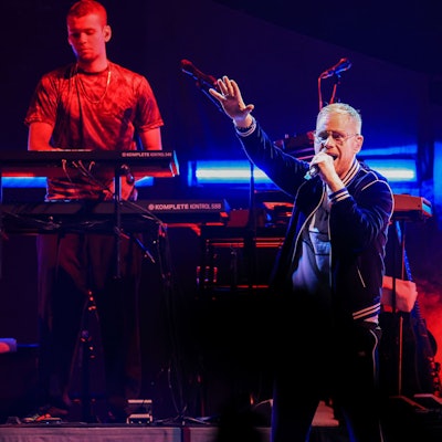 Peter Fox steht singend mit erhobenem Arm auf der Bühne in der Kölner Lanxess-Arena, hinter ihm ein Keyboarder und ein Gitarrist.