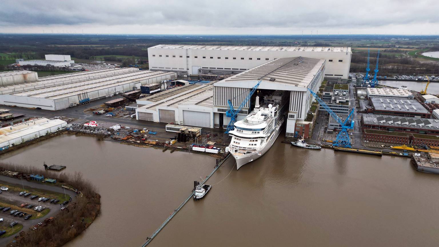 Ein Bild des Geländes der Meyer Werft von oben. Ein Kreuzfahrtschiff verlässt das überdachte Baudock der Meyer Werft.