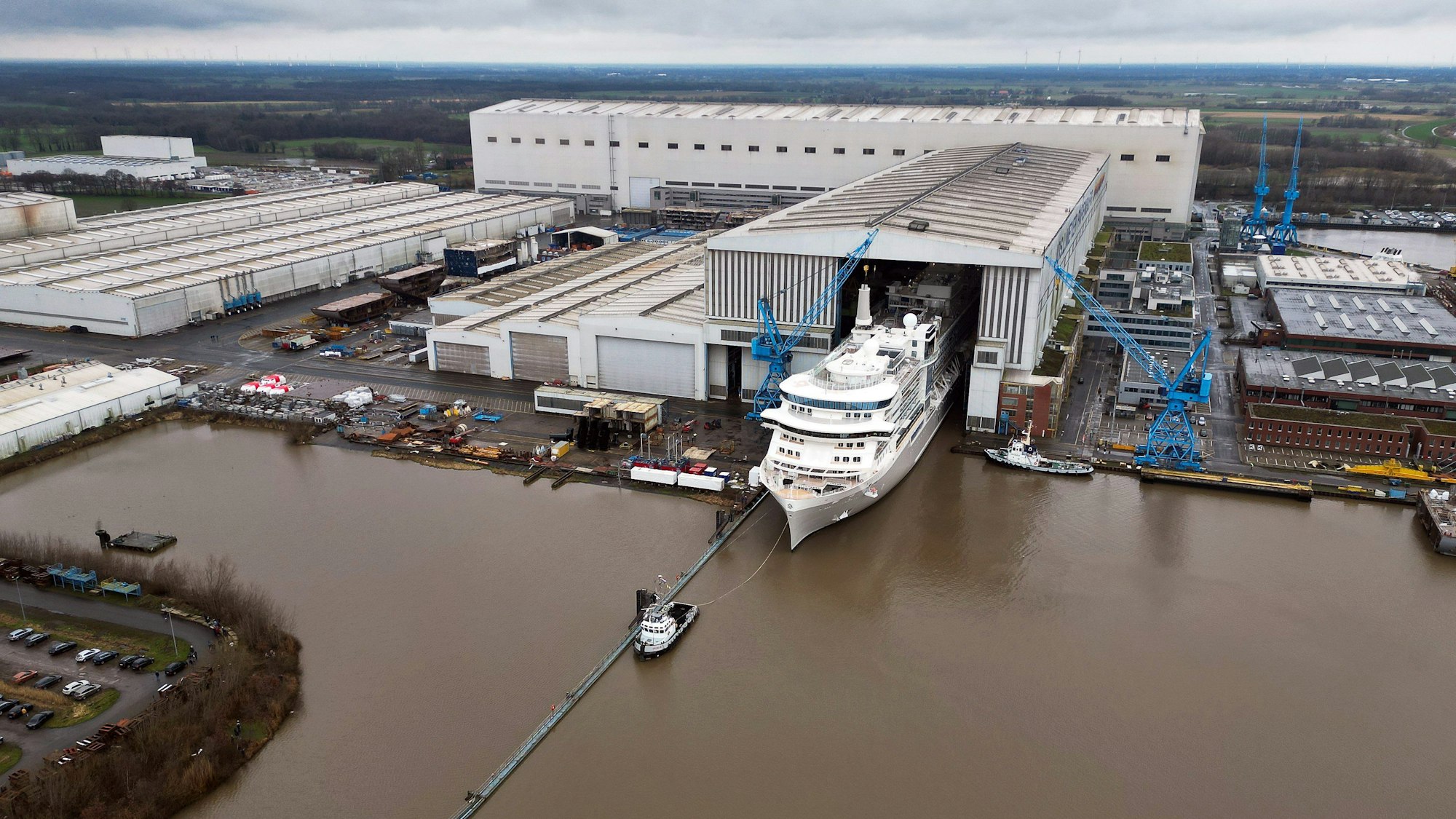 Ein Bild des Geländes der Meyer Werft von oben. Ein Kreuzfahrtschiff verlässt das überdachte Baudock der Meyer Werft.