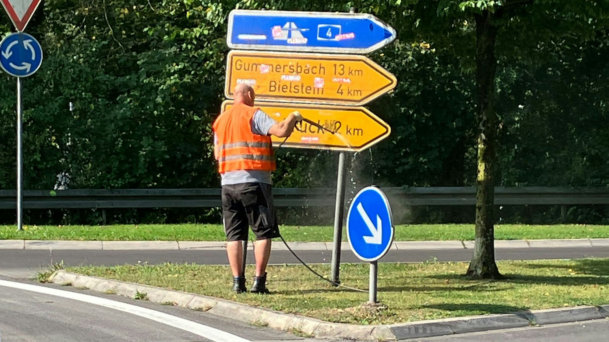 Ein Mann in Warnweste spritzt ein Hinweisschild ab.