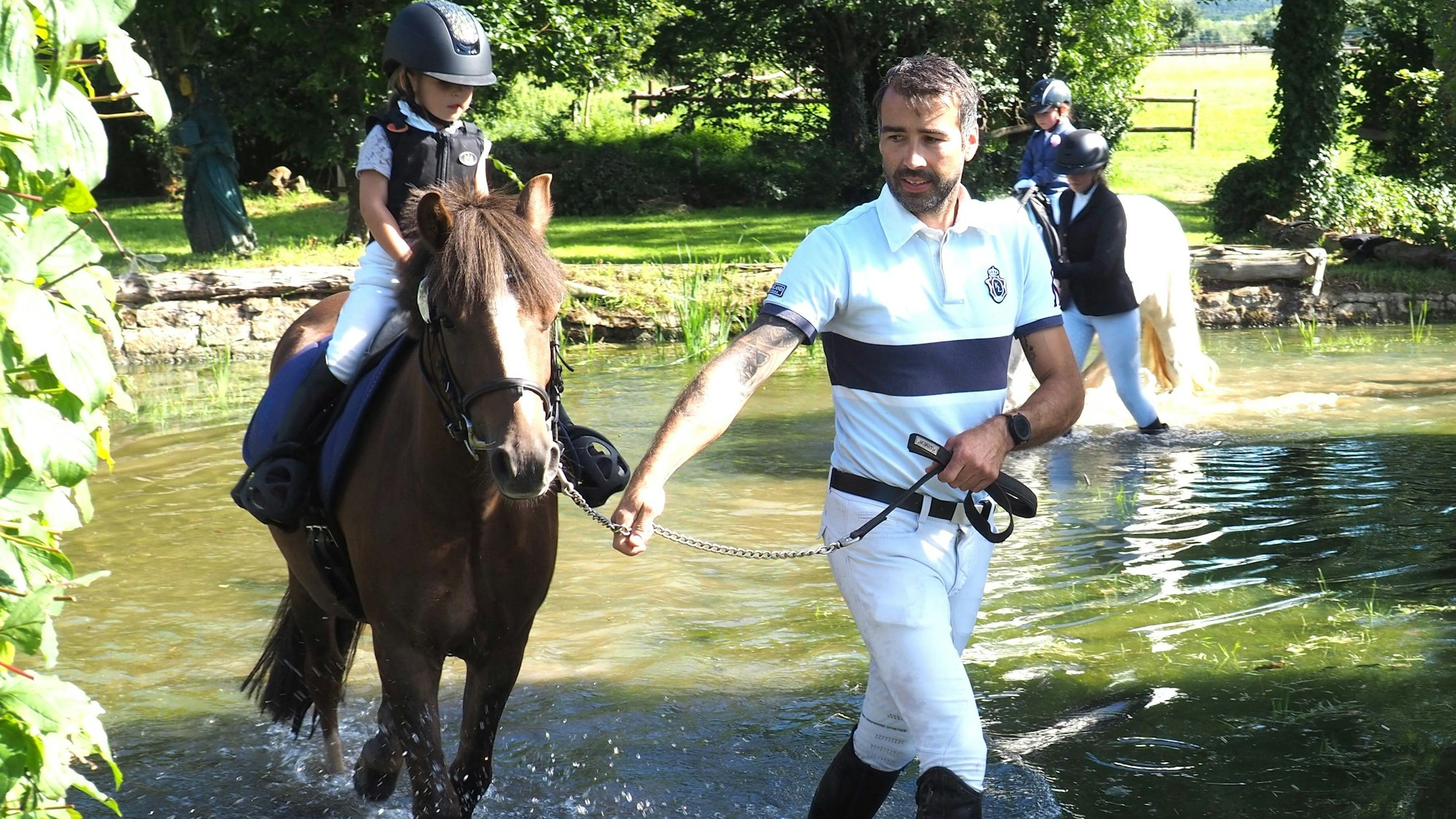 Das Bild zeigt einen jungen Reiter, der auf dem Pferd durch ein Wasserhindernis geführt wird.