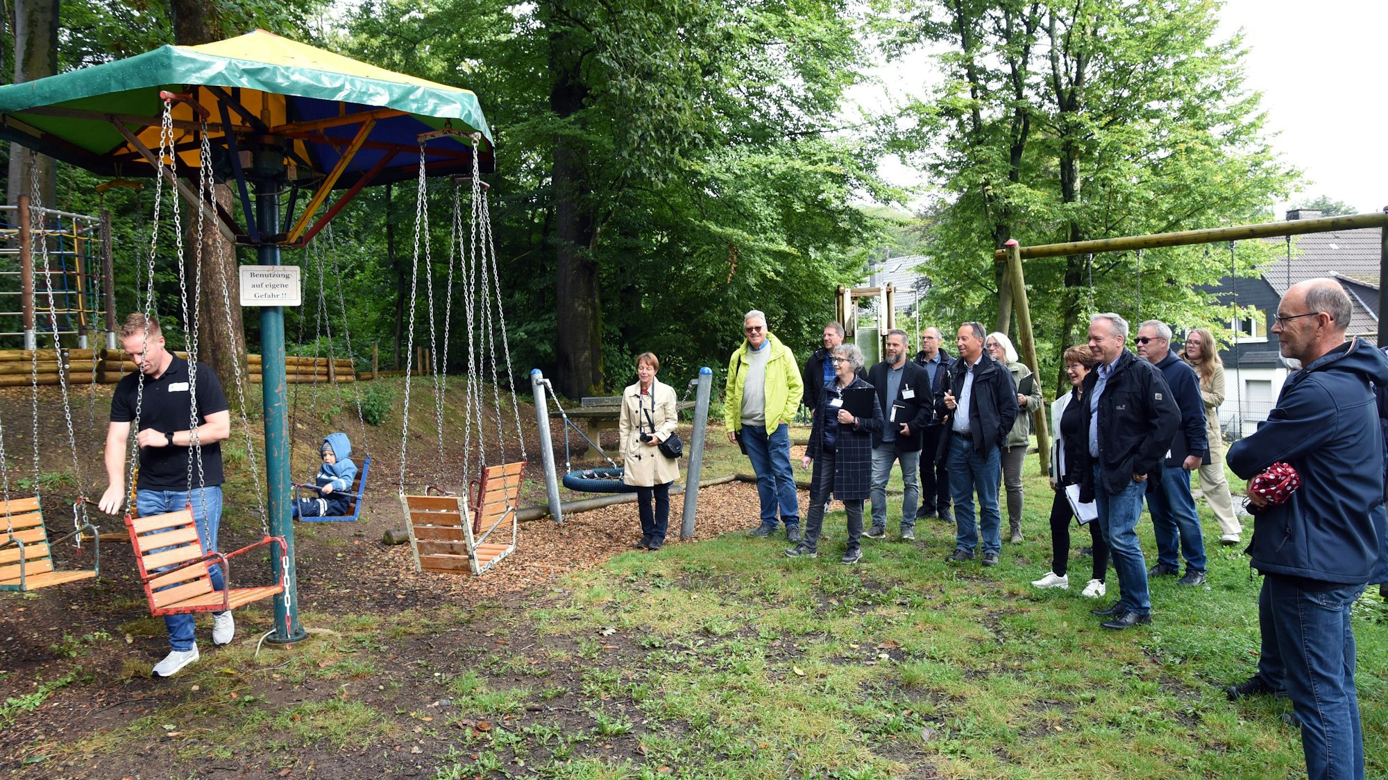 Das Foto zeigt ein Kinderkarussell und eine Gruppe von Erwachsenen.