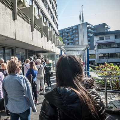 Menschen stehen vor einem Gebäude in einer Warteschlange.