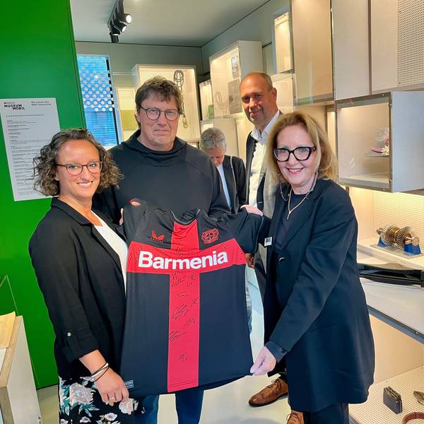 Daniela Frühling (l.) und Rüdiger Vollborn übergeben Gabriele Uelsberg ein Bayer-Meistertikot für das Haus der Geschichte NRW.