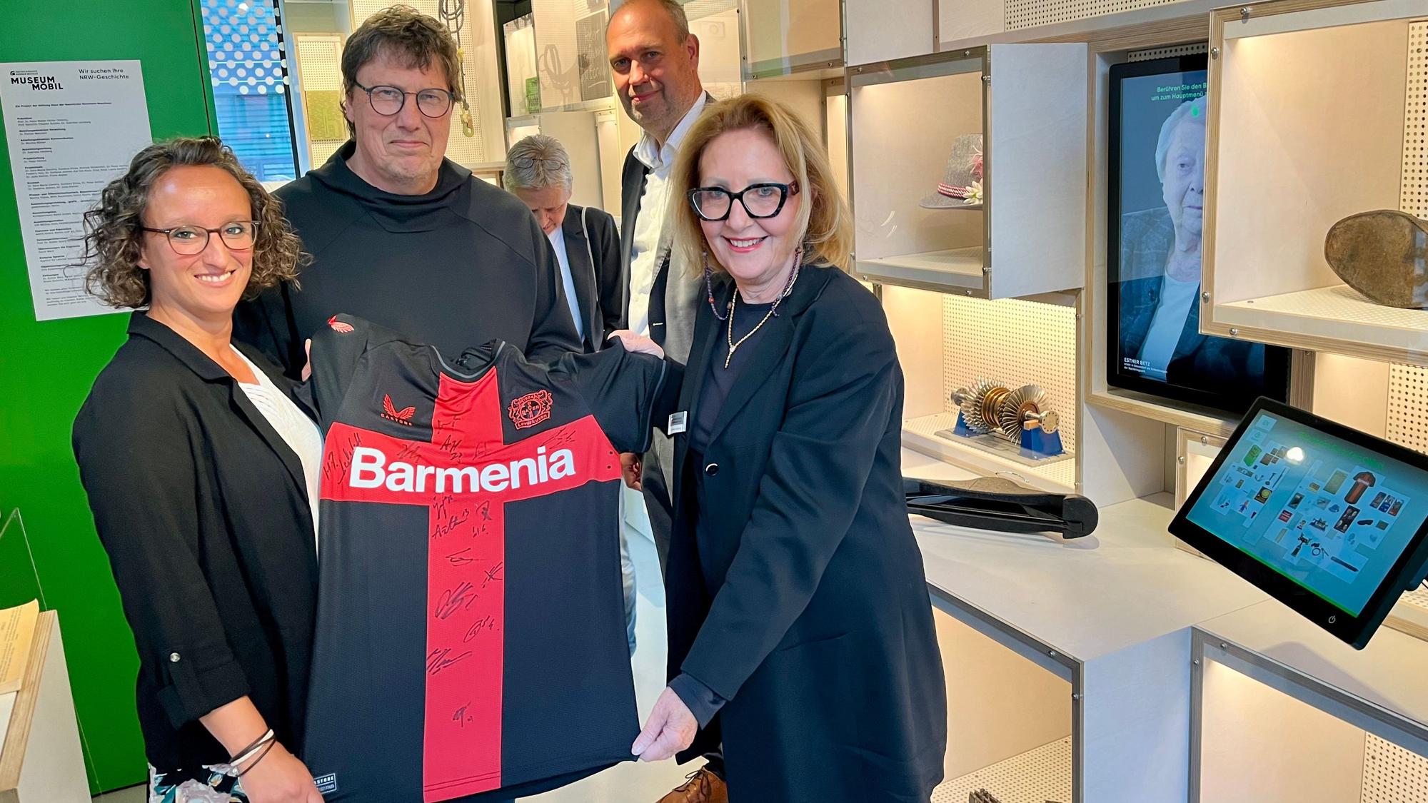 Daniela Frühling (l.) und Rüdiger Vollborn übergeben Gabriele Uelsberg ein Bayer-Meistertikot für das Haus der Geschichte NRW.