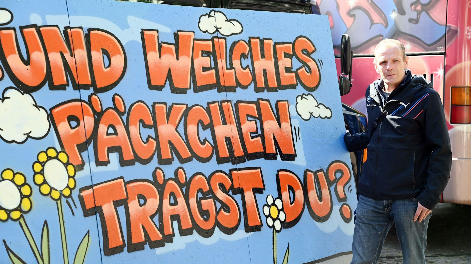 Sebastian Breuer steht neben einem Plakat mit der Schrift „Und welches Päckchen trägst du?“