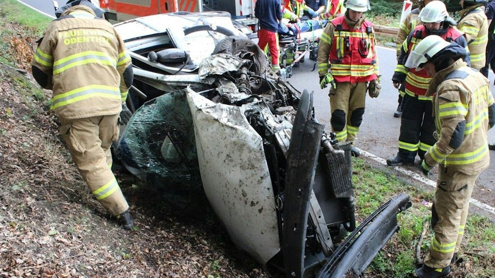 Feuerwehrleute arbeiten an einem Autowrack neben der Landstraße im Scherfbachtal.