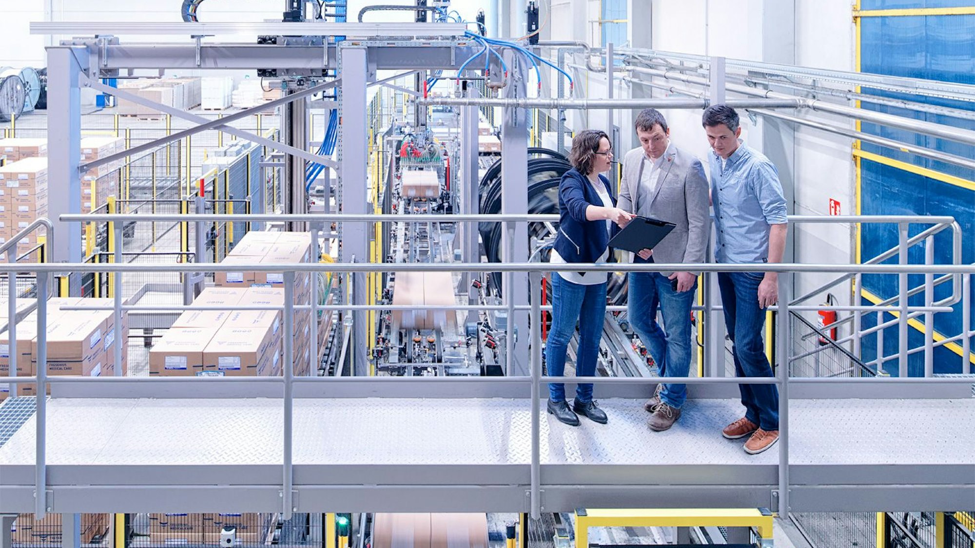 Eine Frau und zwei Männer stehen in einer Fabrikhalle.