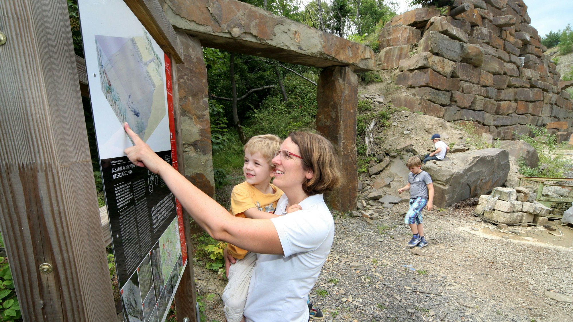 Ein Frau mit Kind auf dem Arm deutet auf eine Tafel.