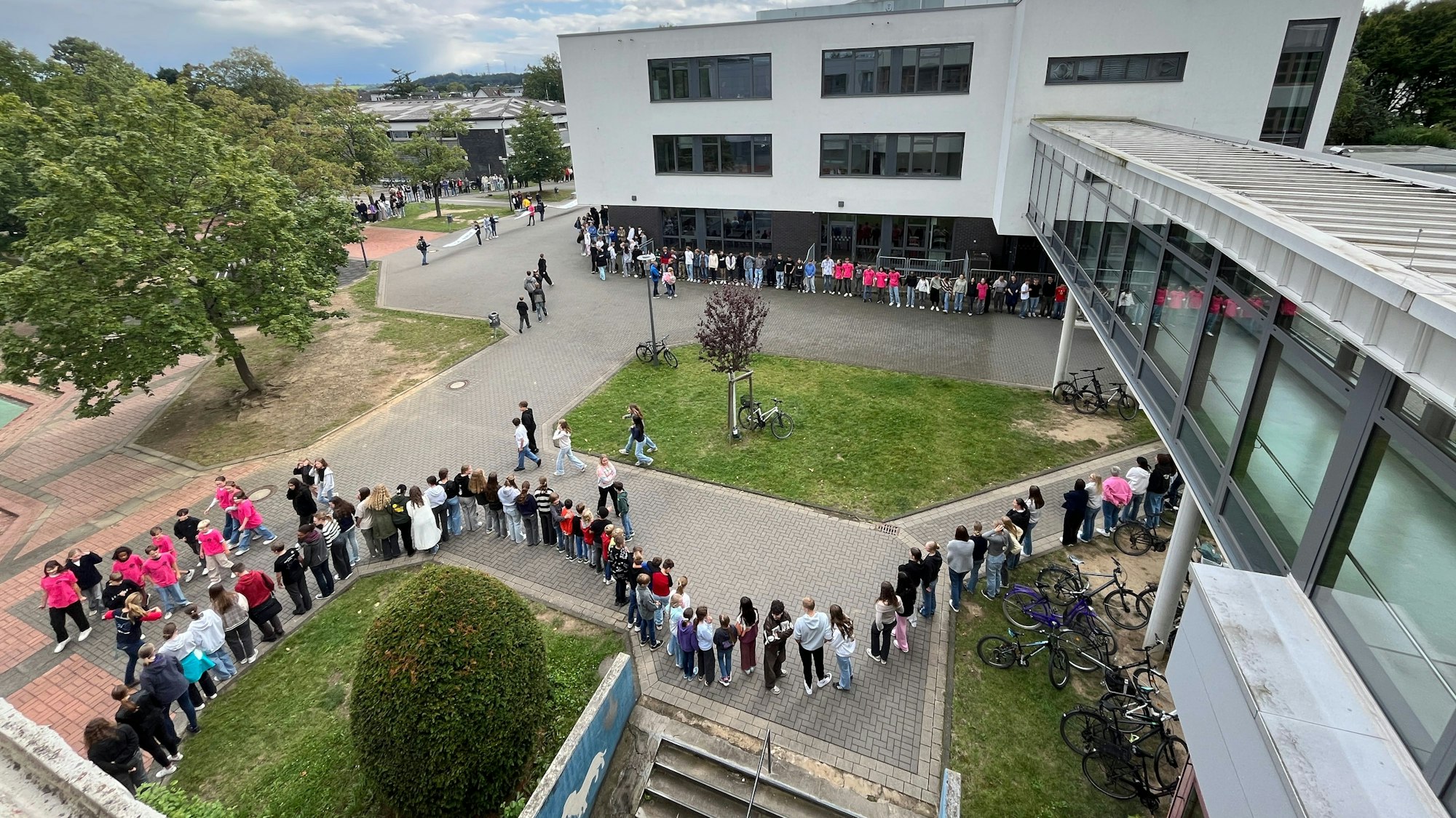 Schülerinnen und Schüler stehen Hand in Hand vor Schulgebäuden.