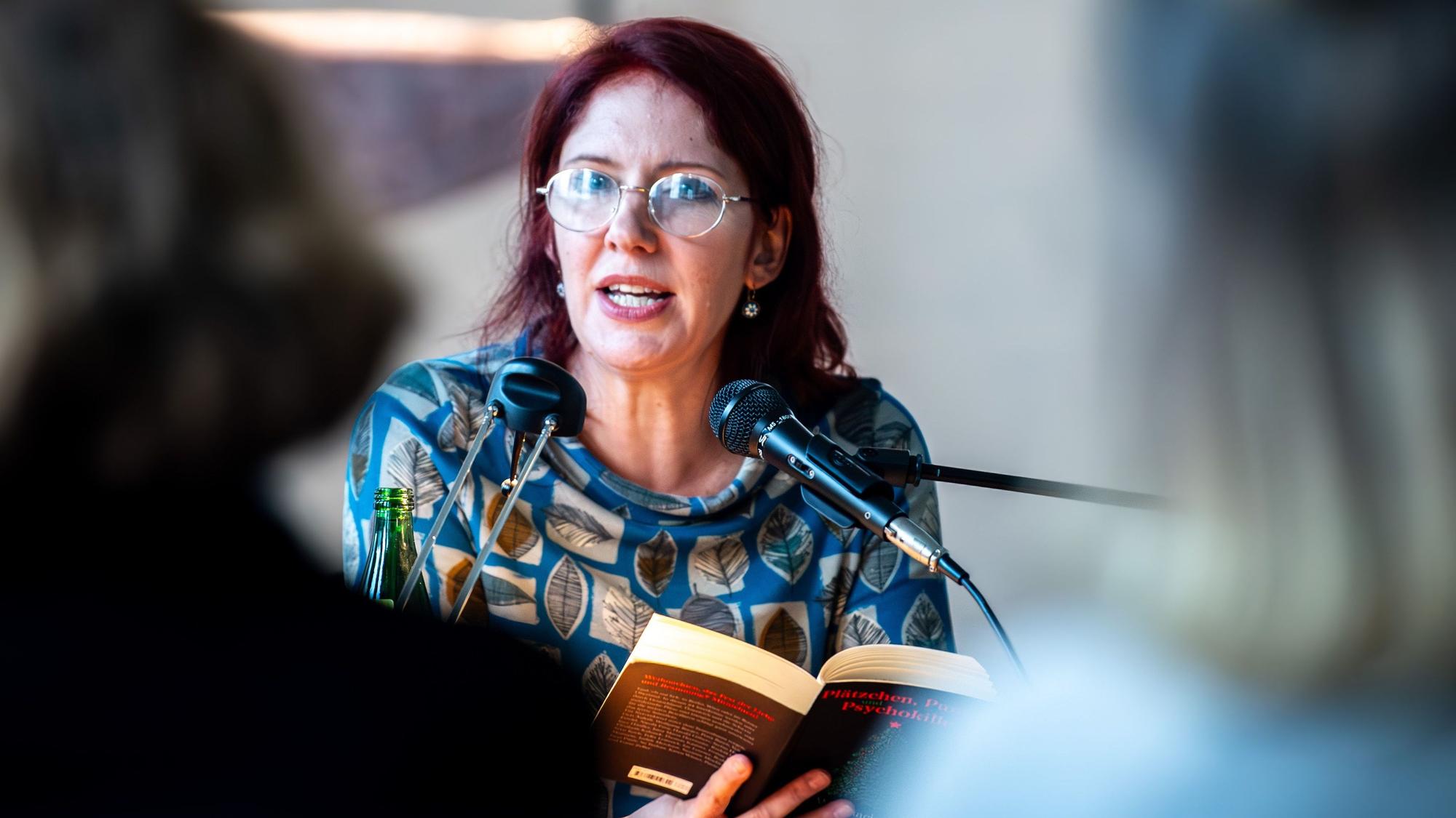 Das Bild zeigt Judith Merchant während der Lesung. Sie hat ein Buch in den Händen.