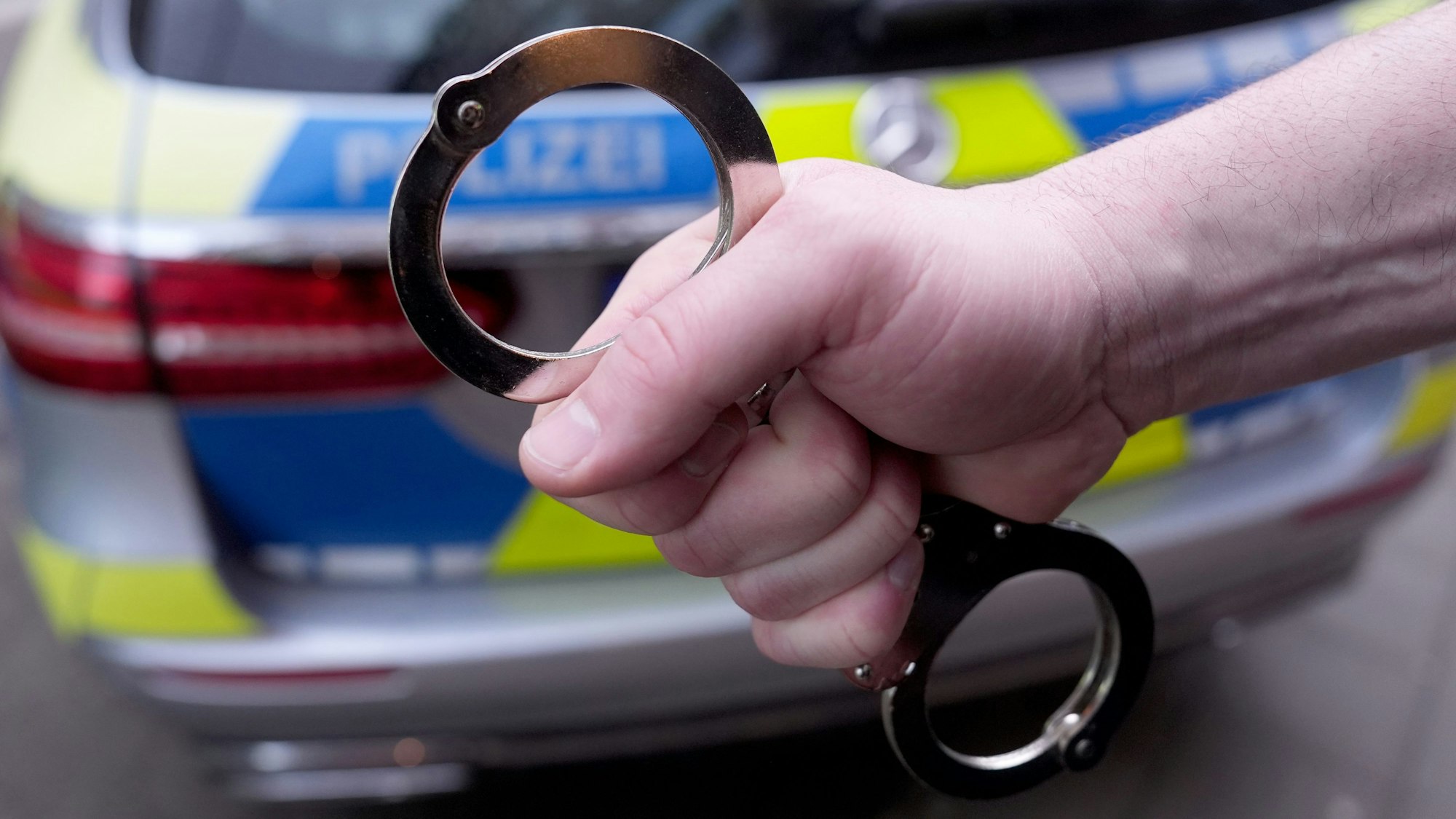 Eine Handschelle vor einem Polizeiwagen