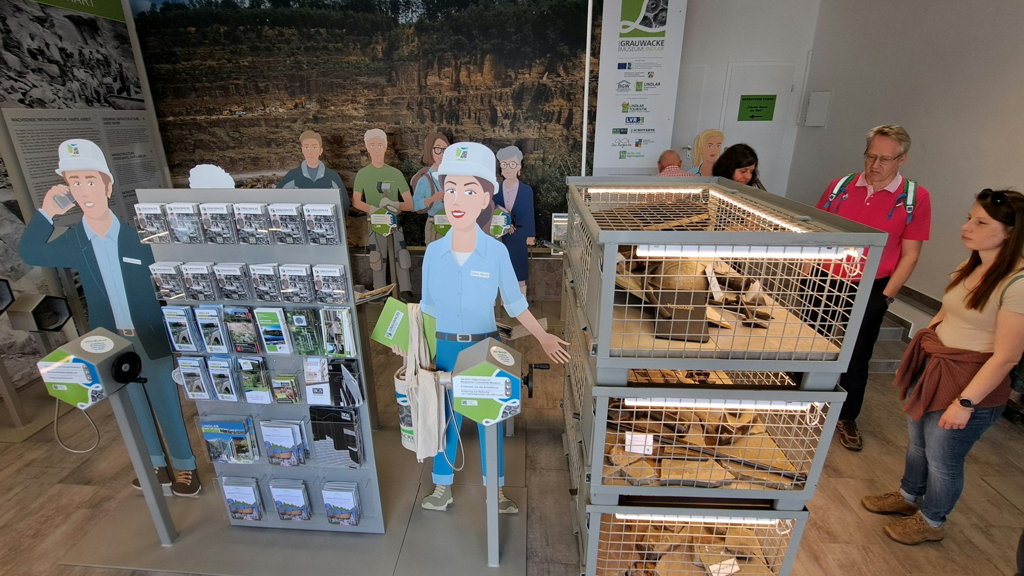 Menschen stehen an Vitrinen und Stahlgitterkisten des Grauwacke-Museums in Lindlar.