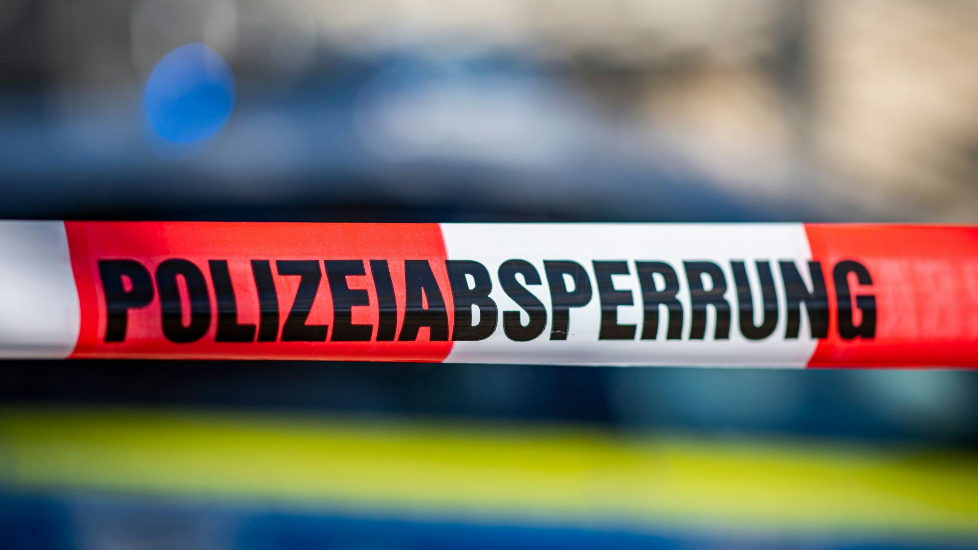 Ein Polizeiabsperrband ist vor einem Polizeifahrzeug zu sehen.