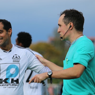 Ein Schiedsrichter und ein Fußballer diskutieren freundlich miteinander.