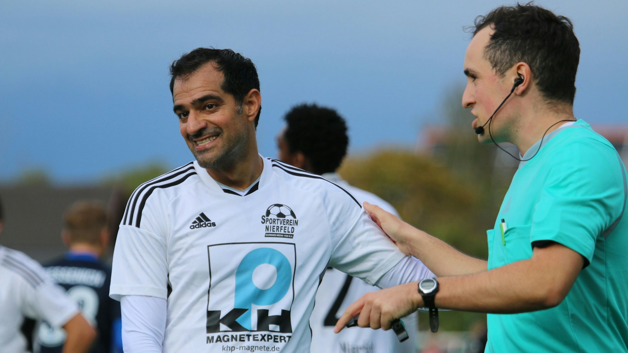 Ein Schiedsrichter und ein Fußballer diskutieren freundlich miteinander.