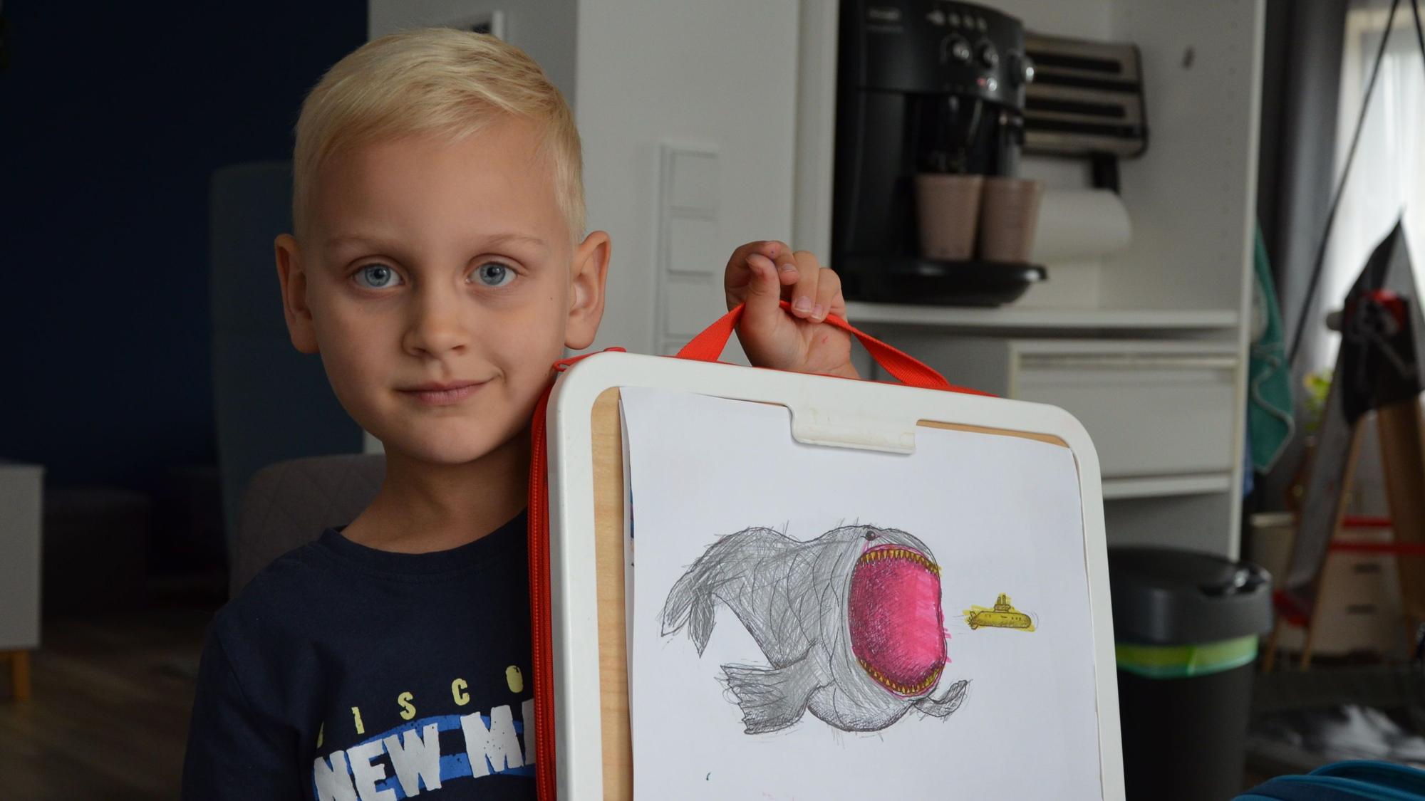 Ein Junge zeigt ein von ihm gemaltes Seemonster.