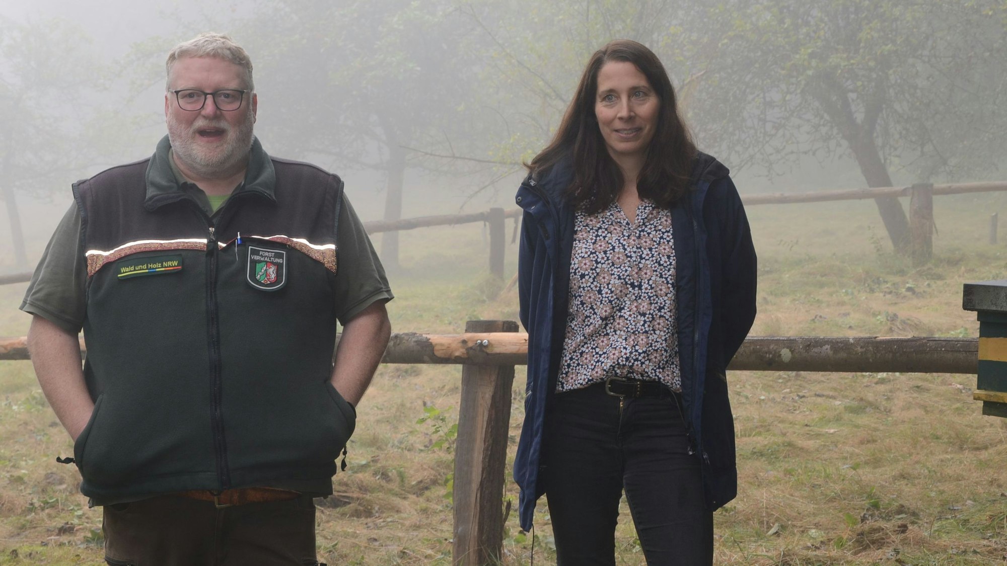 Ein Mann und eine Frau stehen vor einer Streuobstwiese. Das Wetter ist neblig.