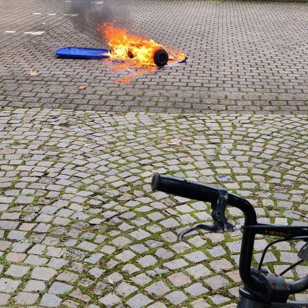 Eine brennende Mülltonne liegt auf einem gepflasterten Platz.