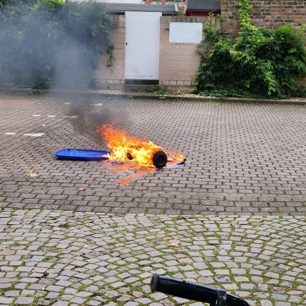 Eine brennende Mülltonne liegt auf einem gepflasterten Platz.